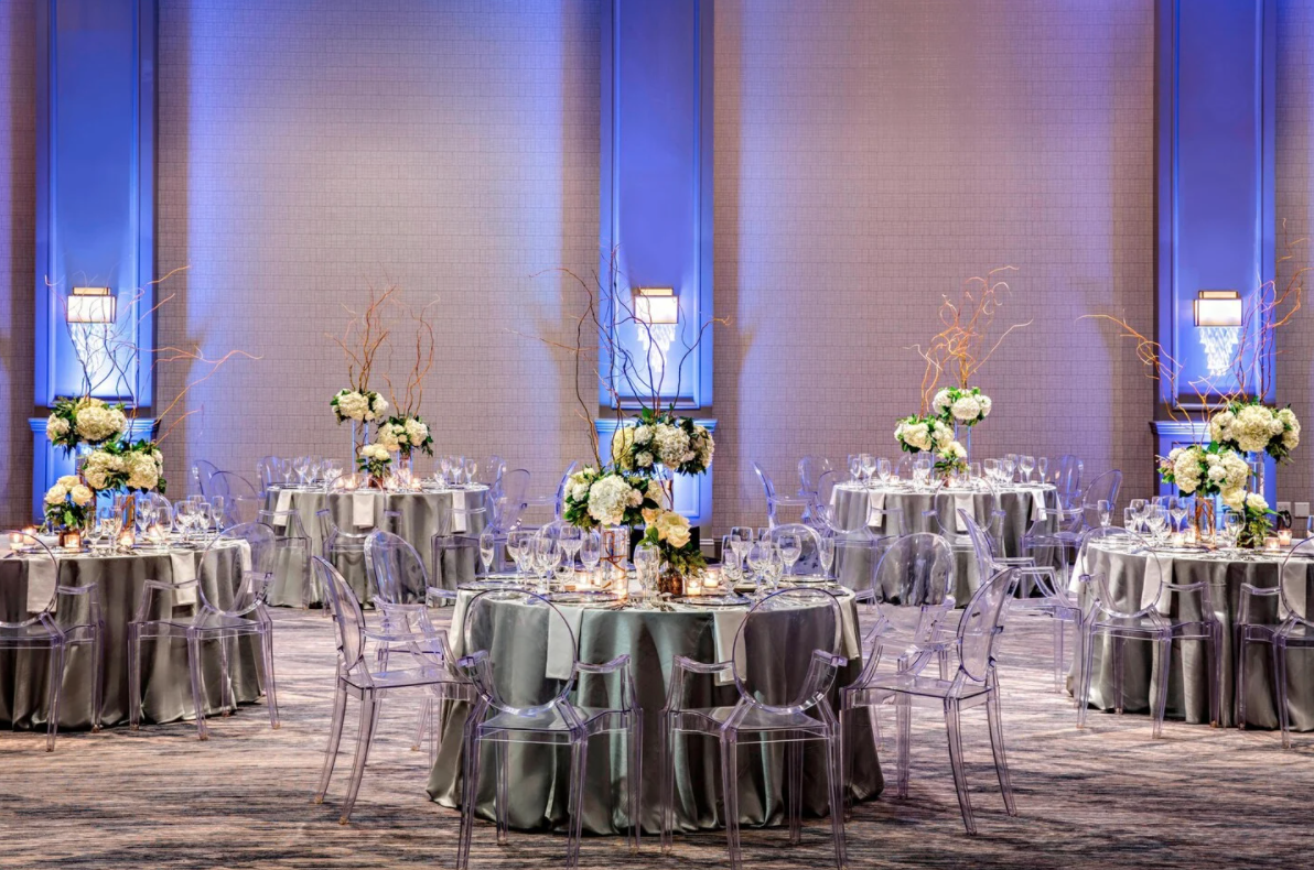 A photo of a ballroom in the JW Marriott Houston by the Galleria, which is decorated with centerpieces consisting of ivory flowers and greenery and silver linens.