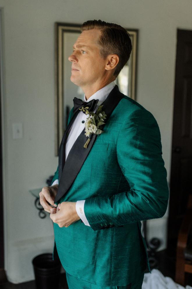 The groom buttons up his emerald green tuxedo. 