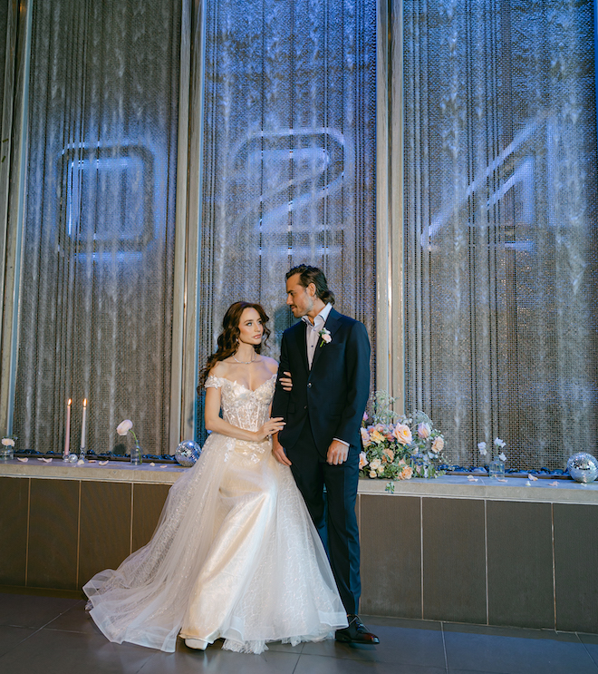 The bride sitting on a ledge holding the groom's arm in front of the 024 Grille water wall. 