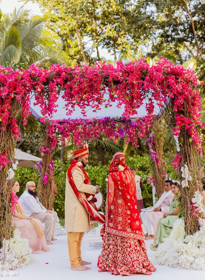 The bride and groom stand under the mandap with vibrant florals at their Indian-fusion wedding in Mexico.