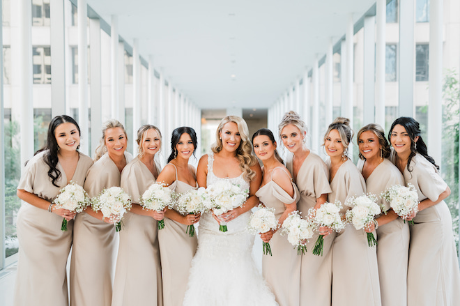 The bride posing with nine bridesmaids in champagne-colored dresses holding white bouquets.