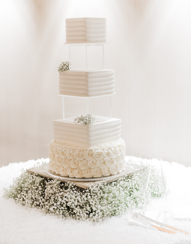 A white wedding cake with acrylic separators in between tiers and decorated with baby's breath. 