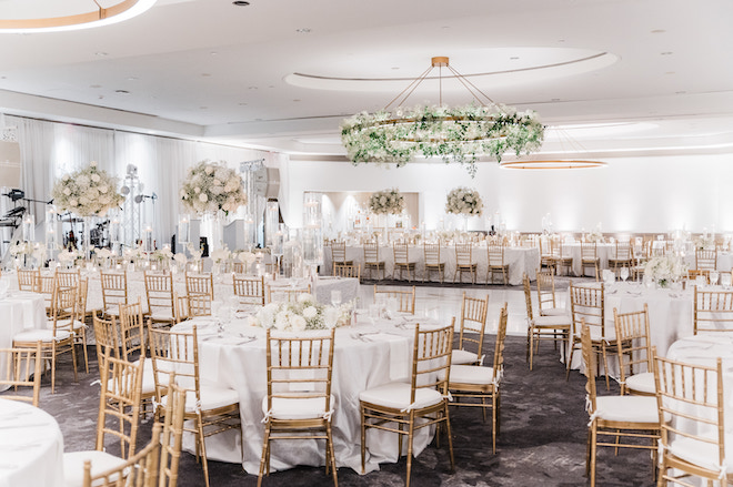 A white ballroom decorated with white florals and gold accents at the C. Baldwin. 