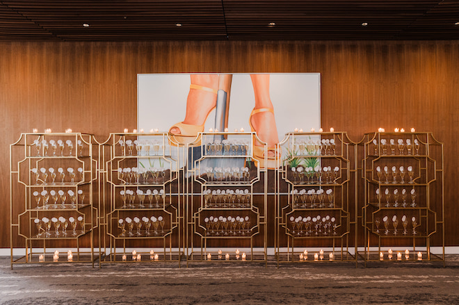 A painting of high heels and 5 gold racks holding champagne.