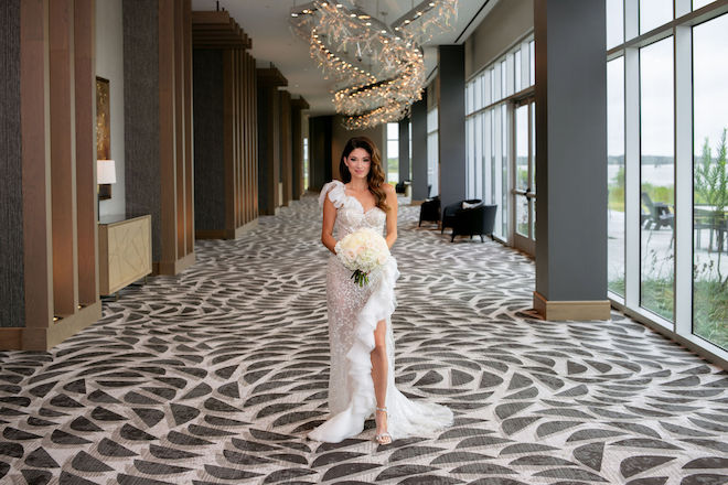 A bride standing in the hallway of Hyatt Regency Baytown Houston, with waterfront views outside of the floor-to-ceiling windows. 