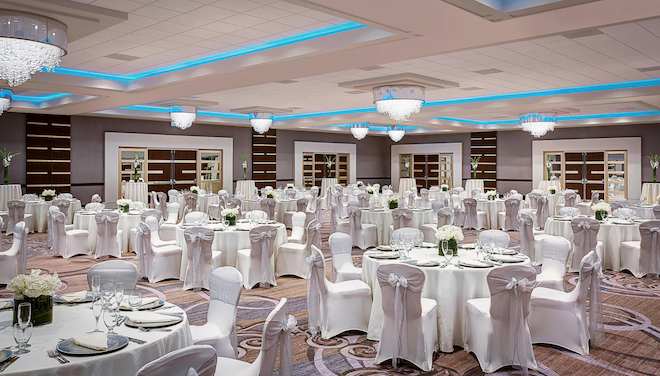 The ballroom of Sheraton Houston Brookhollow Hotel with white round tables and white chairs. 