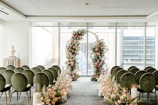 A floral arch and chairs in a ballroom at The Laura Hotel with floor-to-ceiling windows. 