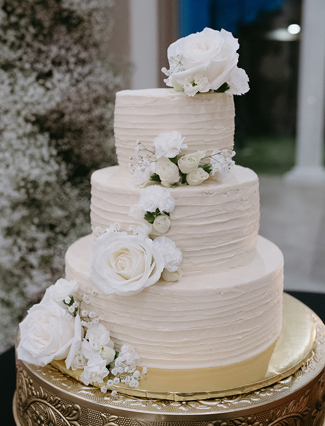 A three-tier white wedding cake with white florals garnishes. 