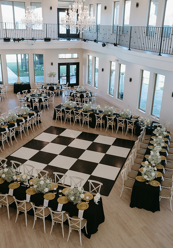 A black-and-white checkered dancefloor with long reception tables covered in baby's breath and gold accents. 