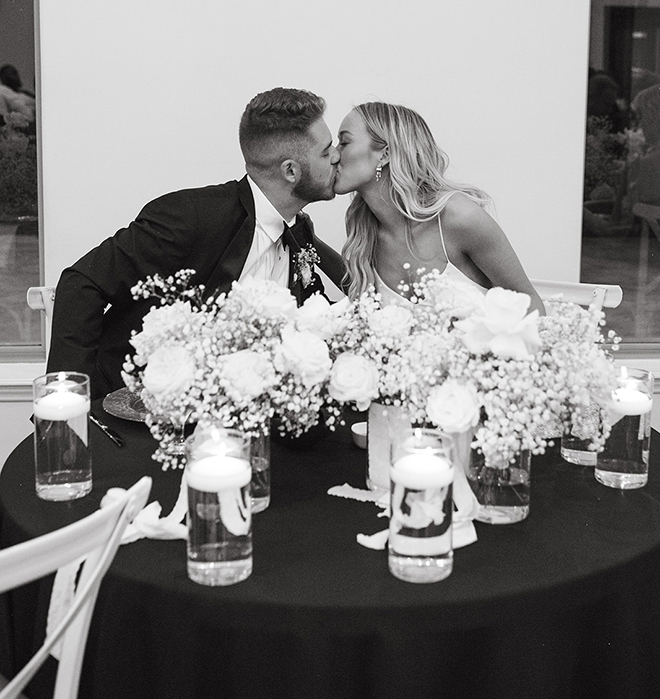 The bride and groom kissing at their reception table. 