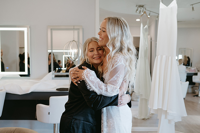 The bride smiling and hugging one of her bridesmaids in the bridal suite. 