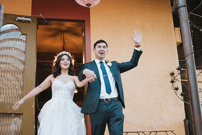 The bride and groom hold hands and celebrate as they walk into their wedding reception.