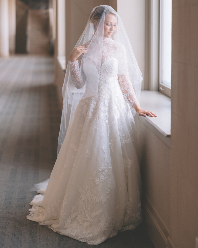 A bride in a long sleeve lace dress with a veil over her head. 