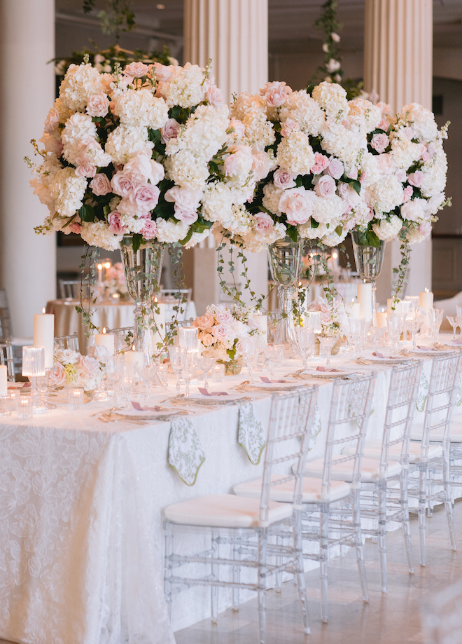 Three large white and blush floral centerpieces on a long reception table. 