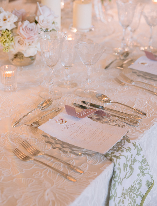 The tablescape with white linens, and a green printed napkin with a white menu. 