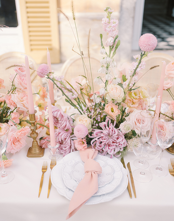 Pink and purple florals with pink candles white plates and gold flatware. 