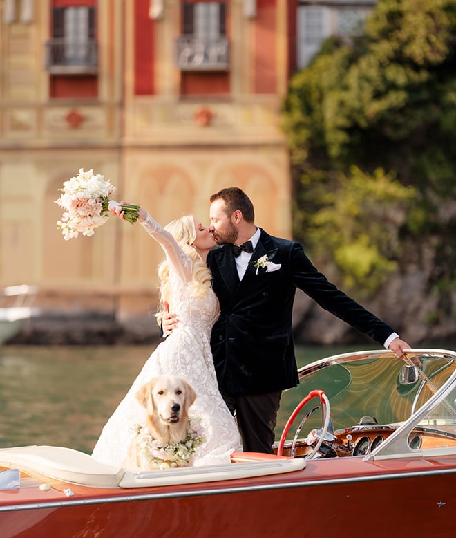 A bride and groom kissing on a red boat with their dog on Lake Como, Italy. 
