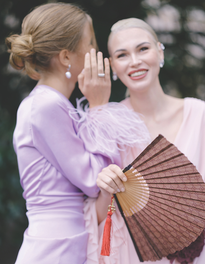 A woman whispering in another woman's ear smiling. 