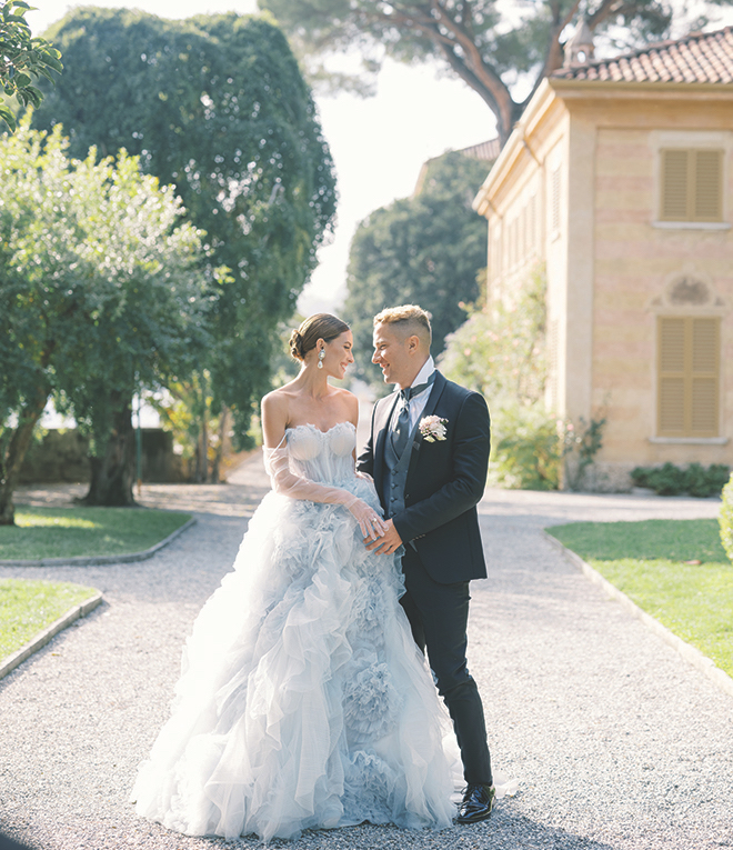 The bride and groom holding hands outside of a building and large trees in Lake Como. 