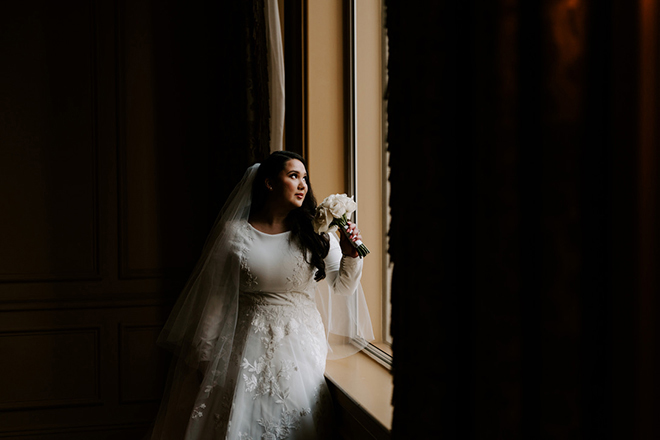 bride in a long sleeve wedding dress looking out a window of Hotel ICON. 