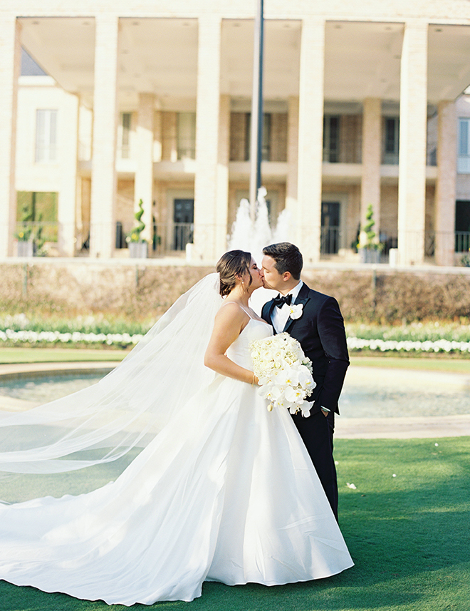 Bride holding a white bouquet while kissing on the lawn of a country club.