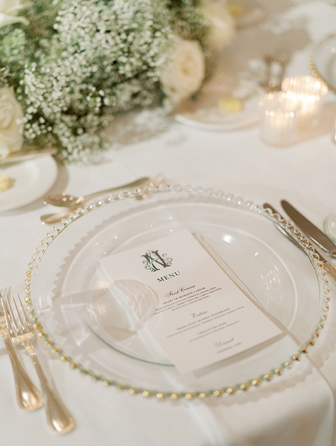 A monogrammed menu on a clear, glass plate.