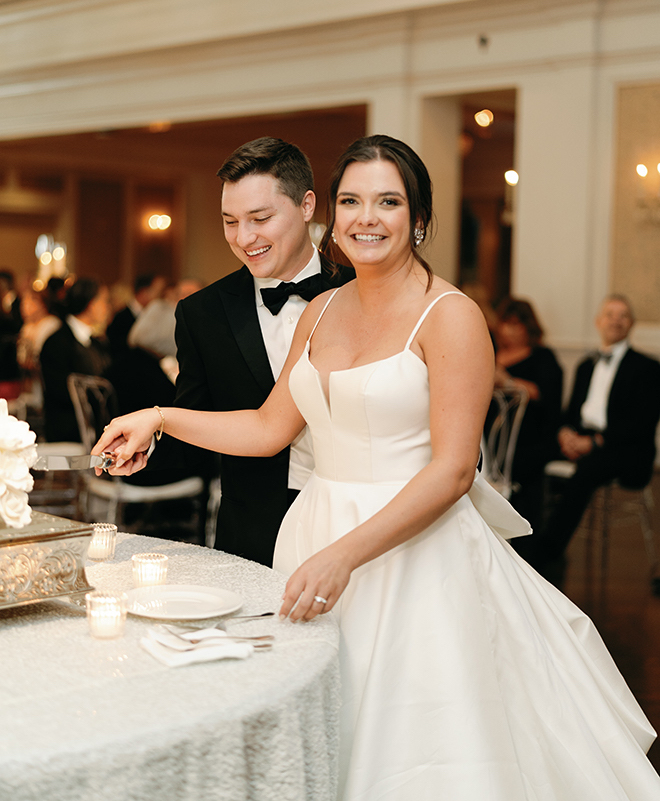 The bride and groom smiling while cutting into their cake. 