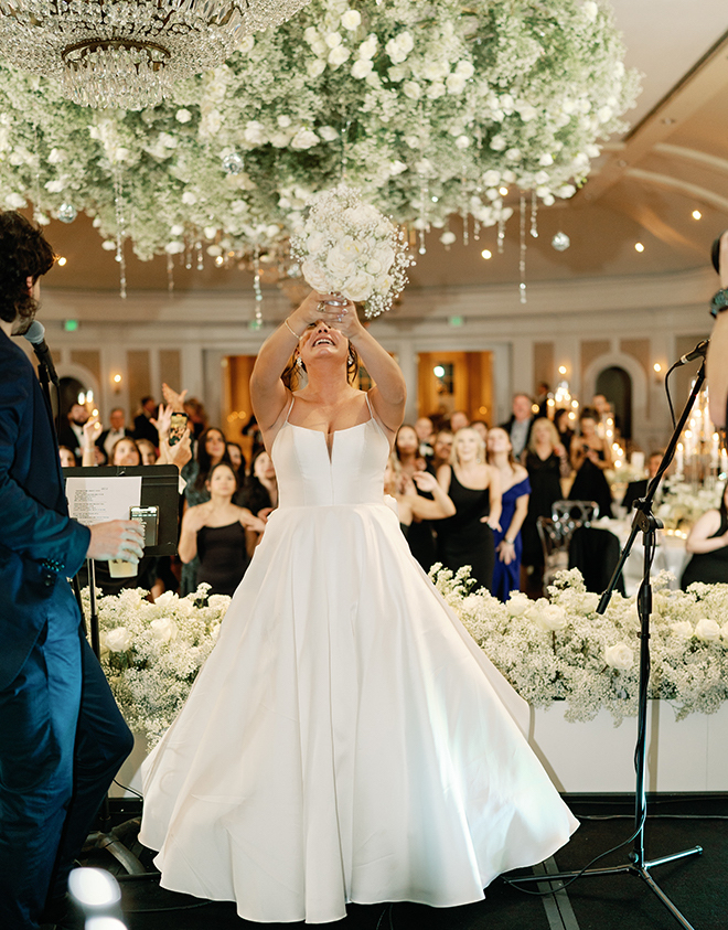 The bride standing on the stage about to throw the bouquet behind her. 