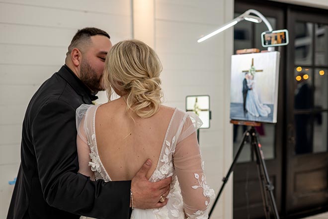 The couple share a kiss as they react to their wedding day painting by live wedding painters Rendered Moments.