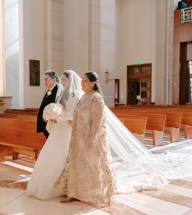 The bride walking down the aisle in a church with her parents. 