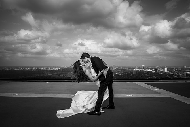 The groom dips the bride while kissing her on the helipad of The Post Oak Hotel at Uptown Houston.