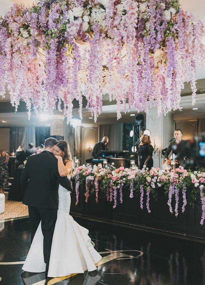 The bride and groom hugging during their first dance under a floral canopy and Danny Ray and The Atlantic Street Band on the stage. 