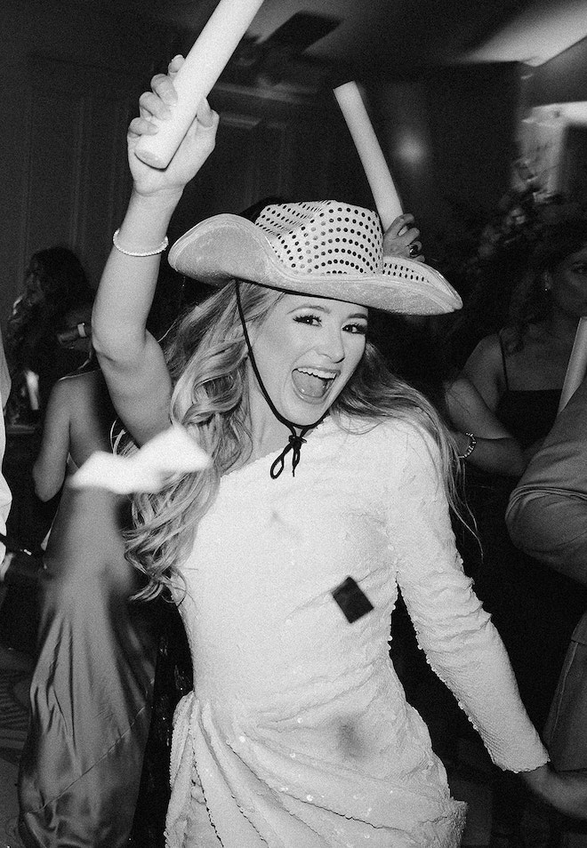 A bride wearing a sequined cowboy hat and holding a glow stick during the reception. 