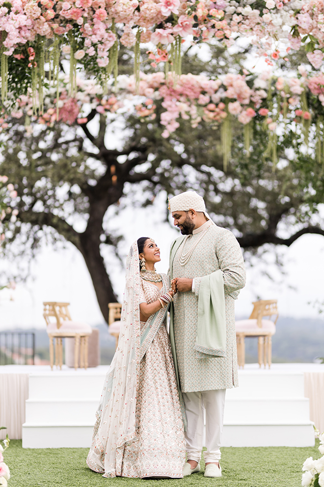 Bride and groom smiling at each other under a mandap covered in pink flowers and greenery at Omni Barton Creek Resort & Spa.