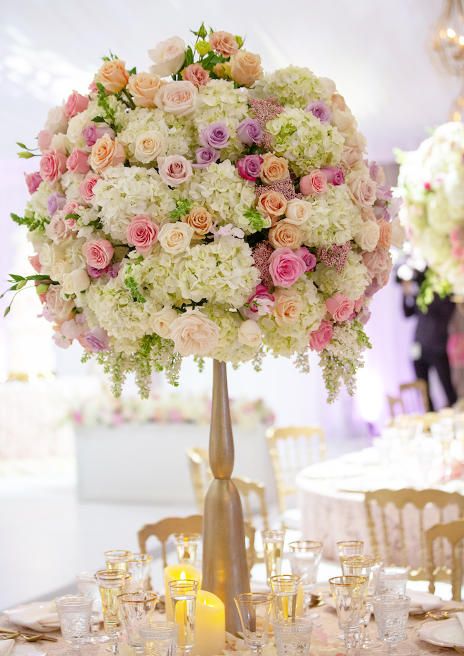 A grand floral arrangement on white hydrangeas, purple, orange and pink roses. 