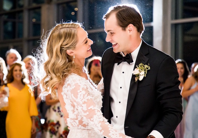 The bride and groom smile at each other while they dance at their wedding reception.