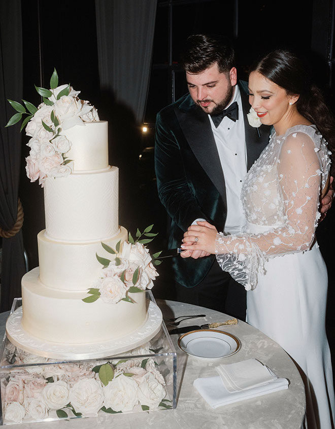 The couple slice into their 4-tier white wedding cake designed by Cakes by Gina.