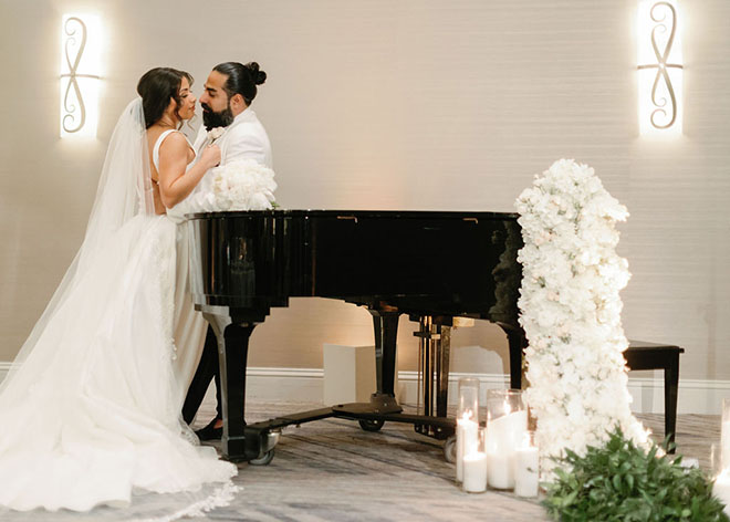 The bride and groom stand next to a piano in the ballroom.