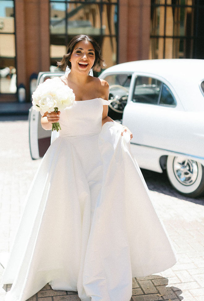 The bride stands outside of the JW Marriott Houston by The Galleria next to a white vintage car.