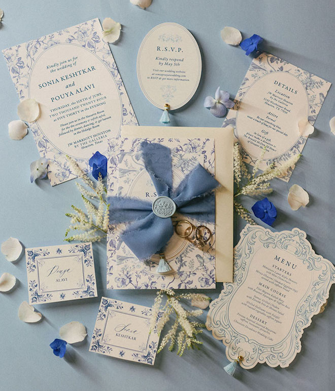 Blue and white wedding stationery are surrounded by blue and white flower petals.