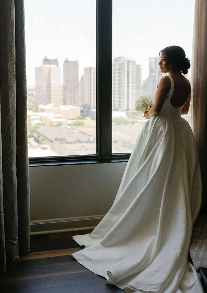 The bride looks out of a window in the penthouse suite overlooking the city of Houston.