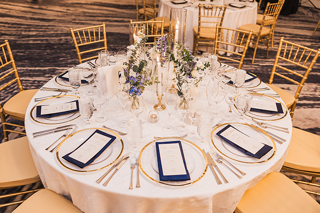 At the reception party, the table is detailed in blue and golds. Tables are set with a menu and utensils. 