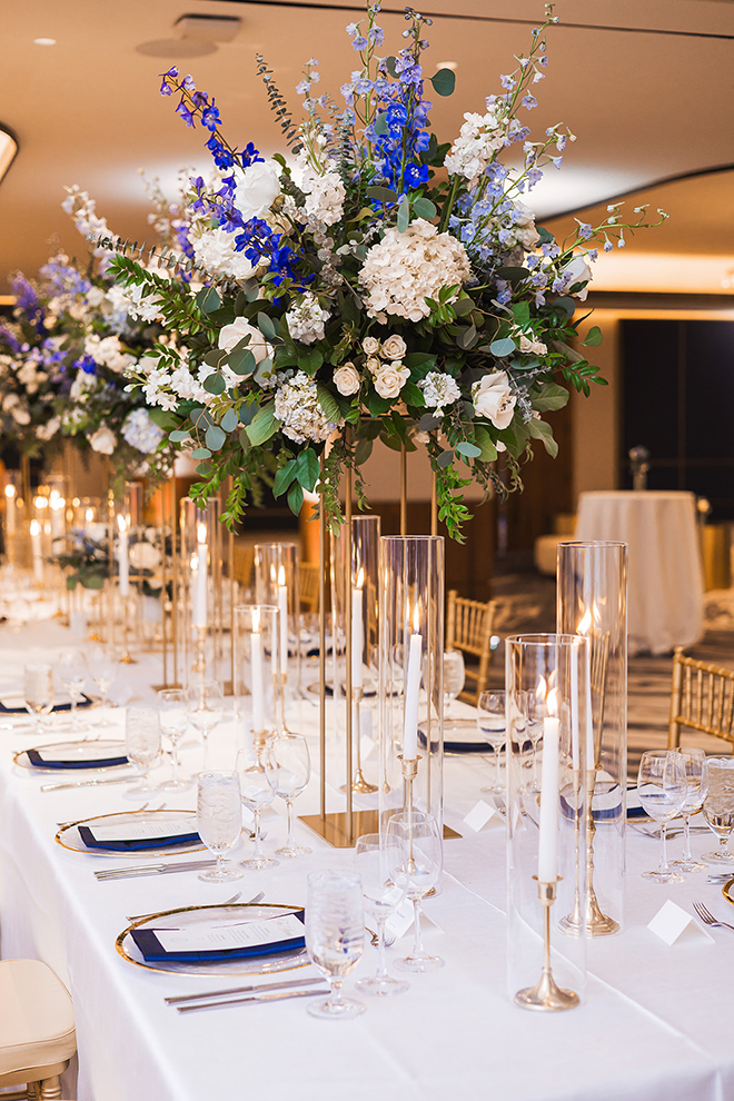 The bridal party table is long with large blue and white bouquets covering the table along with candles. 