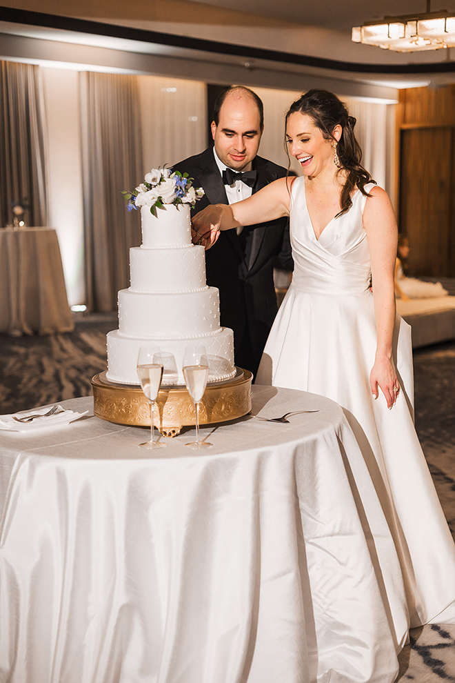 The bride and groom cut their white wedding cake during their celebration. 