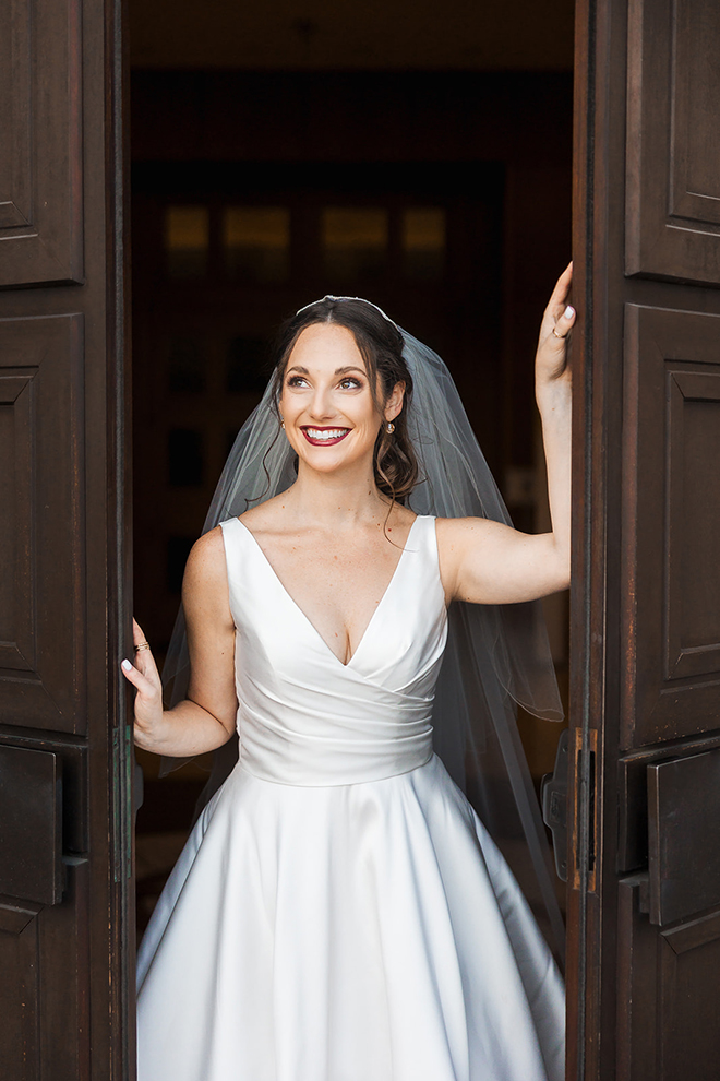 The bride poses for a photo in her wedding dress and veil at the chapel. 