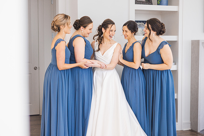 The bride stands in the middle of her bridesmaids as they are dressed in blue gowns. 