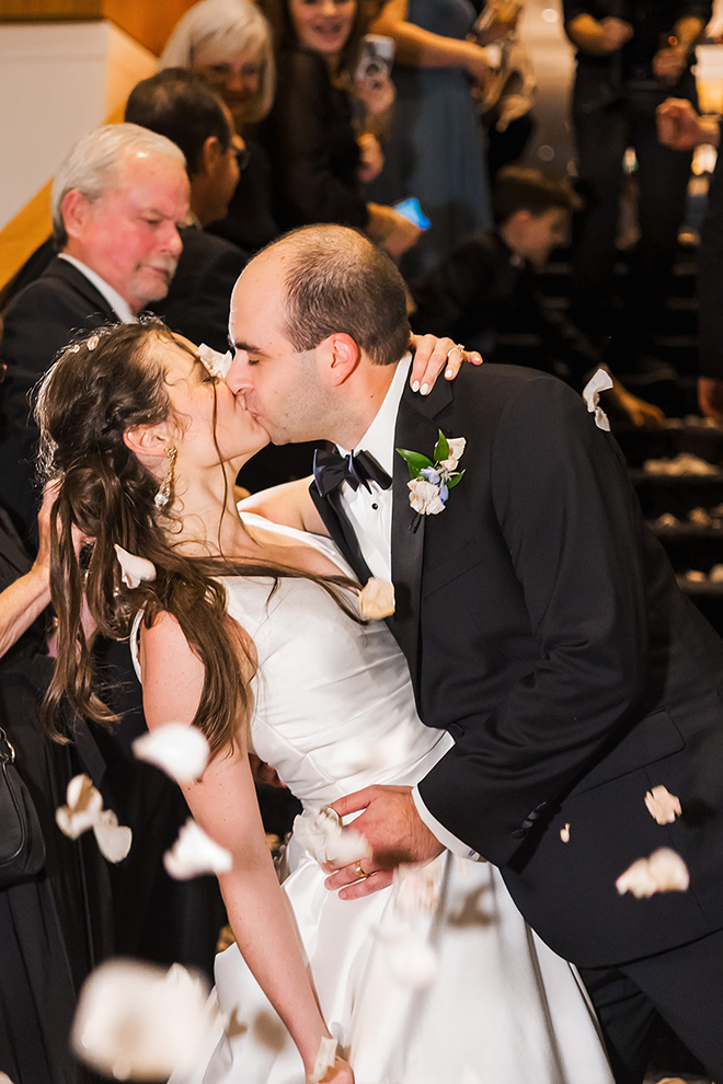 The bride and groom get sent off with rose petals and applause as they leave the reception kissing. 