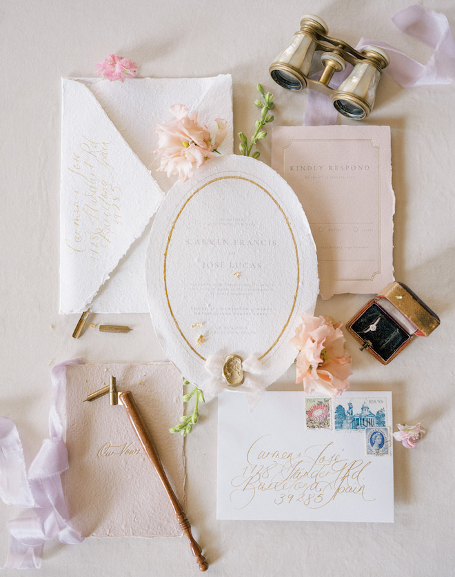 A flat lay of the wedding invitation with decorations of florals, ribbon, and wedding rings. 