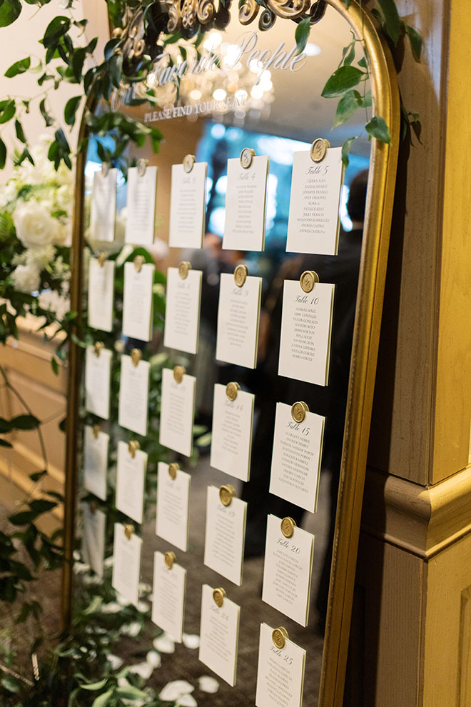 A gold trimmed mirror is the seating chart for the beachside wedding. 