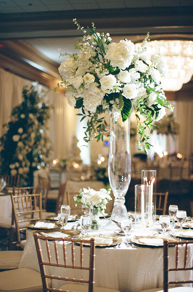 White flowers and greenery are placed in floral arrangements for the reception tables.